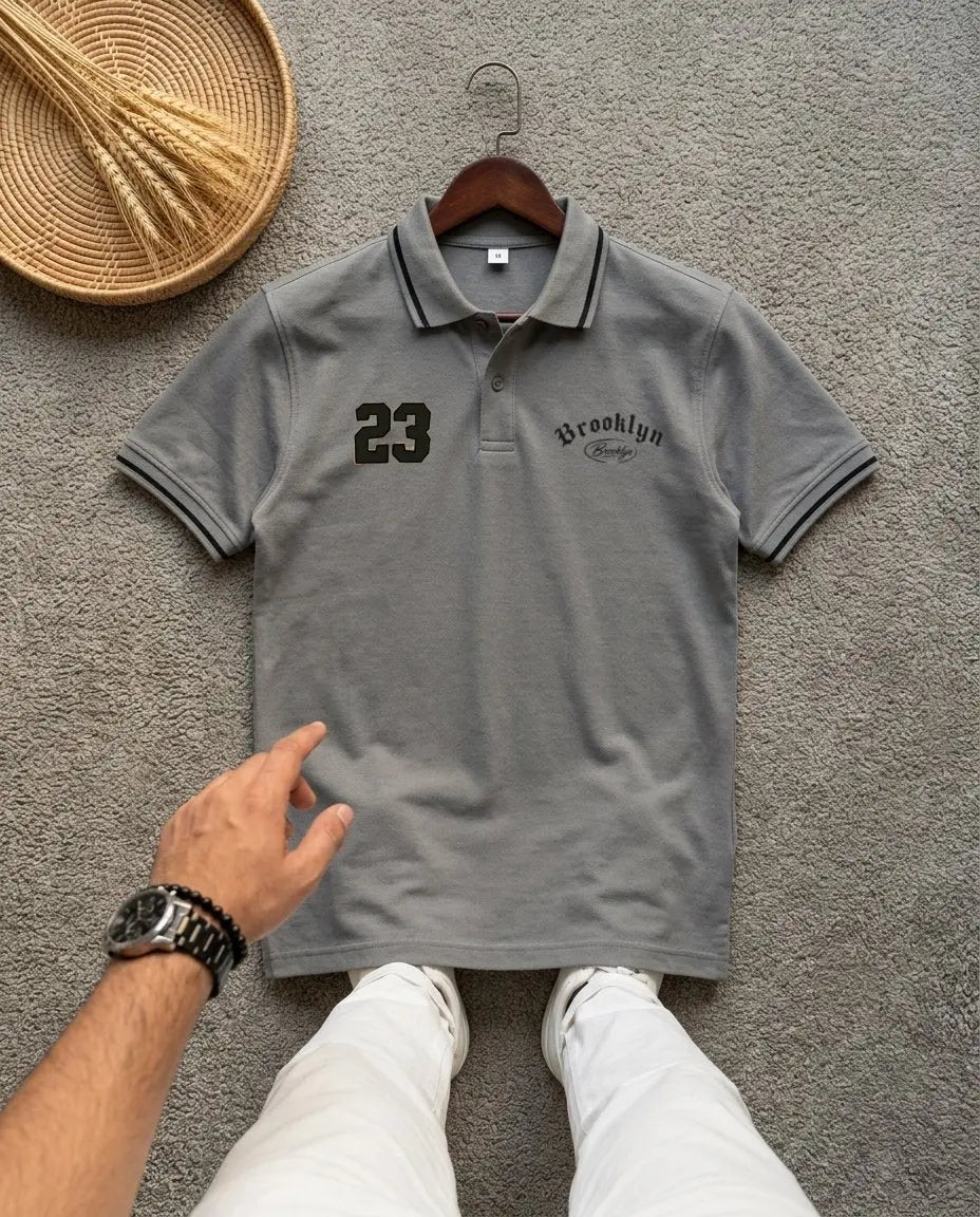 Grey polo t-shirt with 'Brooklyn 23' print and striped collar on a grey background